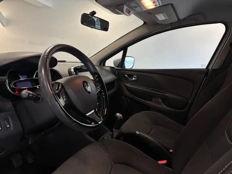 Intérieur avant droit de la Renault Clio gris Platine 2014, volant cuir avec commandes et boîte manuelle visible.