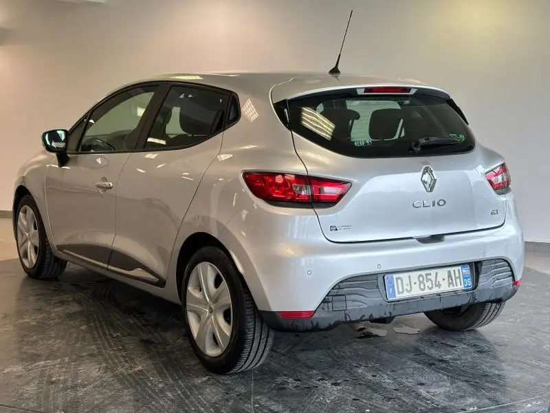 Renault Clio gris platine vue 3/4 arrière droit, avec feux arrière allumés et jantes alu visibles.