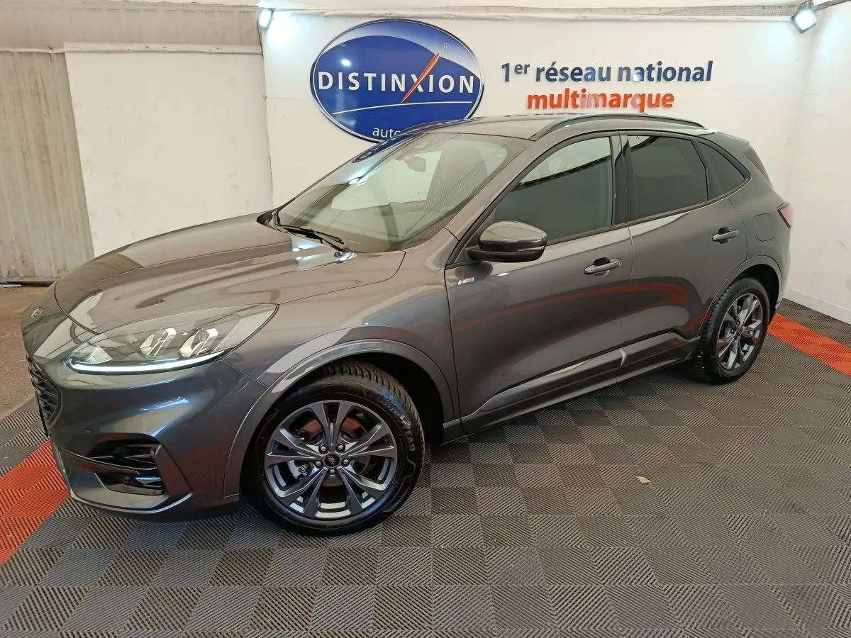 Ford Kuga gris clair en vue 3/4 avant droit, avec jantes alliage et toit noir dans un showroom intérieur.