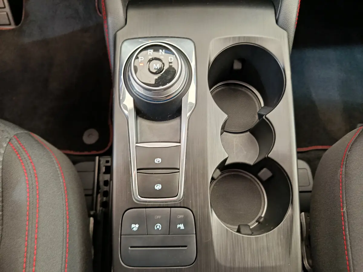 Vue plongeante sur la console centrale noire du Ford Kuga gris clair, avec molette de boîte auto et porte-gobelets.