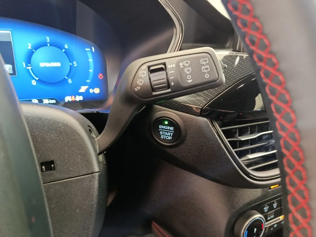 Gros plan sur le bouton start/stop et le combiné d'instruments bleu du Ford Kuga gris clair, intérieur côté conducteur.