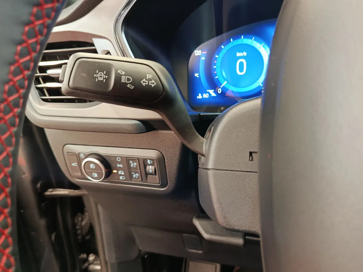 Gros plan sur le commodo gauche et le tableau de bord numérique bleu du Ford Kuga 2024 gris clair, intérieur moderne.