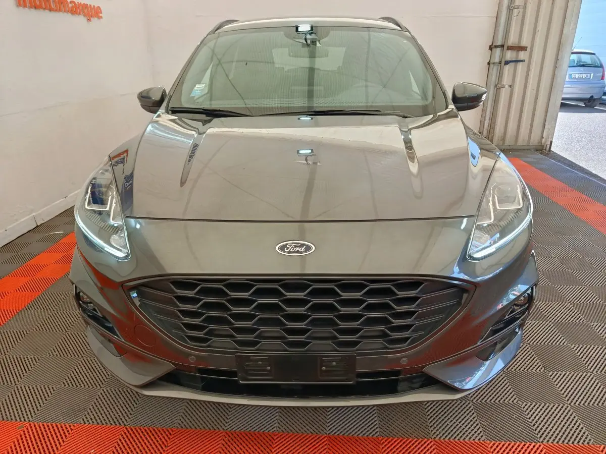 Vue frontale d'un Ford Kuga gris clair 2024 avec calandre hexagonale et phares LED allumés