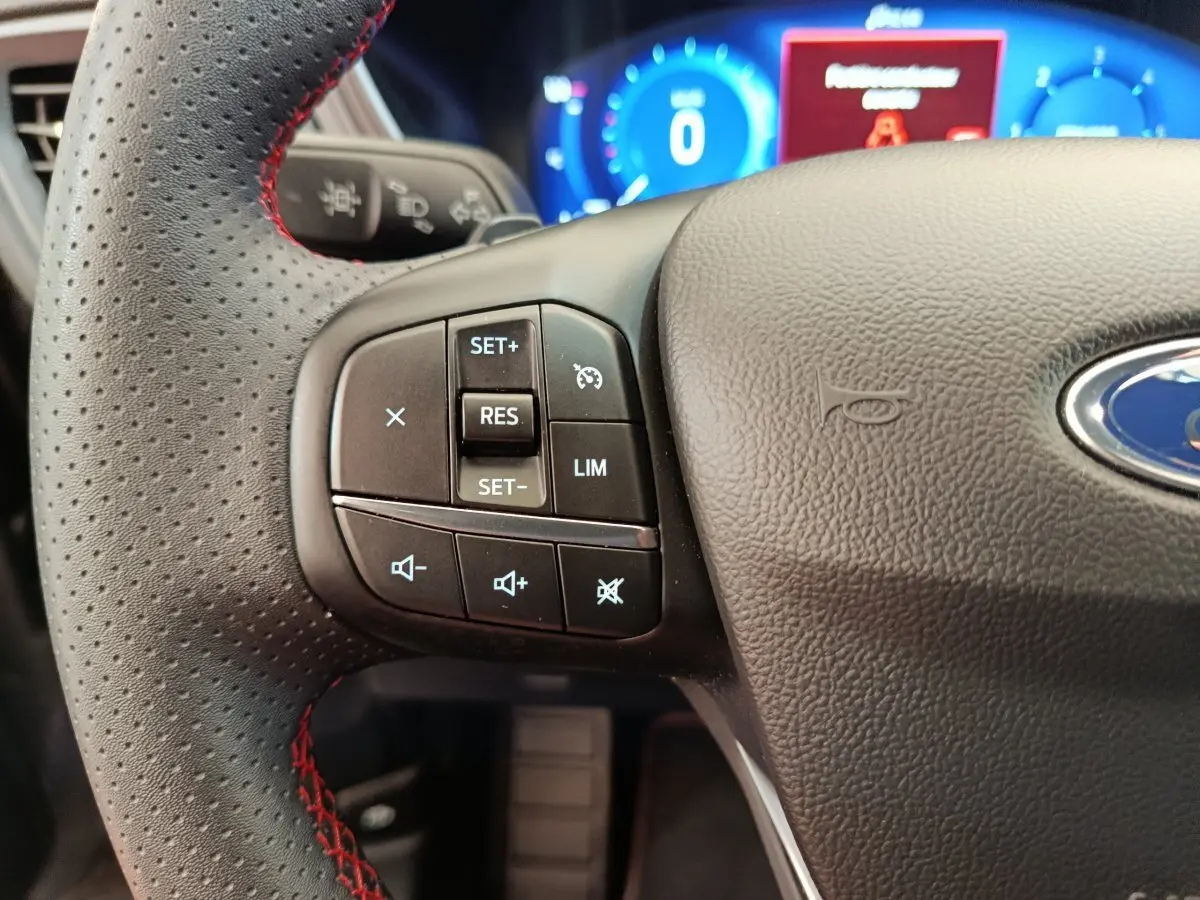 Gros plan sur le volant cuir perforé avec surpiqûres rouges du Ford Kuga 2.0 EcoBlue 2024, affichage digital en arrière-plan.