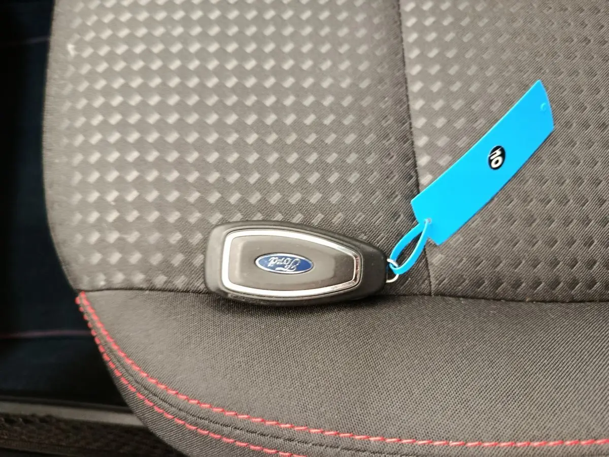 Clé Ford posée sur siège tissu gris foncé avec surpiqûres rouges, intérieur du Ford Kuga 2024 visible partiellement.