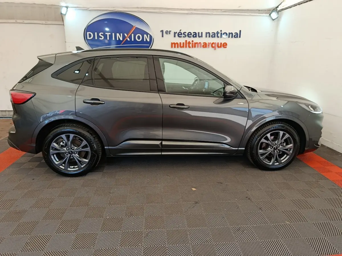 Ford Kuga 2024 gris clair vue de profil côté gauche dans un showroom avec jantes alliage et vitres teintées