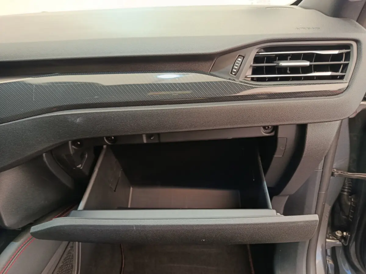 Gros plan sur la boîte à gants ouverte côté passager du Ford Kuga 2024 avec tableau de bord noir et insert carbone.