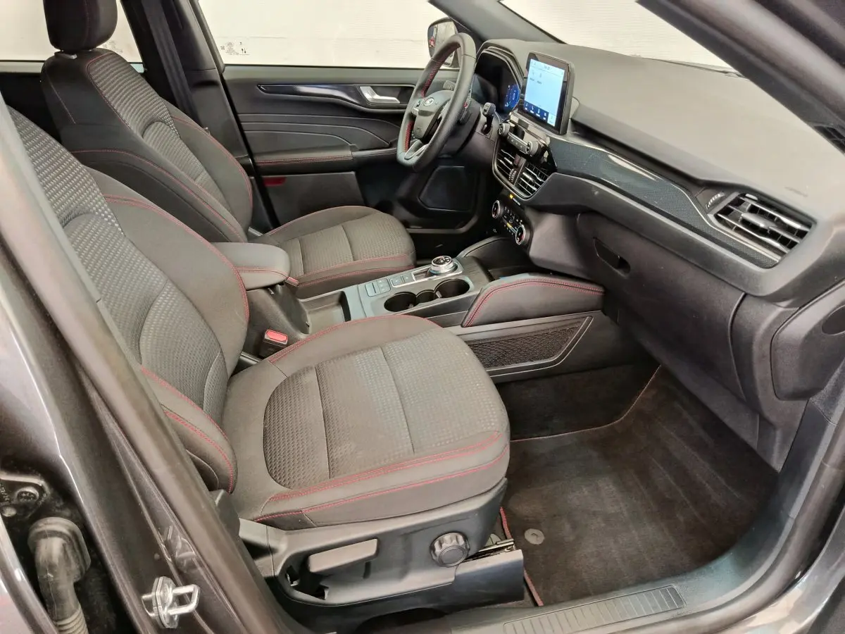 Intérieur avant droit du Ford Kuga gris clair 2024, sièges tissu avec surpiqûres rouges et écran tactile central.