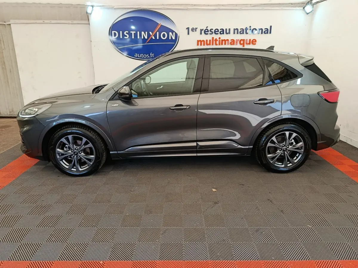 Profil côté gauche d'un Ford Kuga gris clair 2024 St Line, posé en intérieur sur sol damier avec logo Distinxion en arrière-plan.