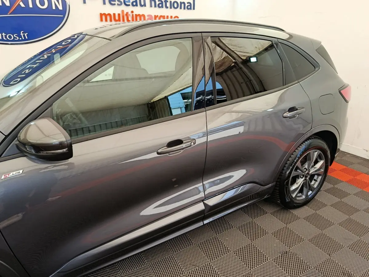 Vue latérale côté gauche d'un Ford Kuga gris clair finition ST Line avec jantes alliage et vitres teintées.