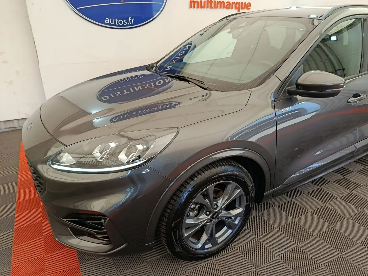 Vue 3/4 avant droit d'un Ford Kuga gris clair avec phares LED et jantes alliage au showroom.