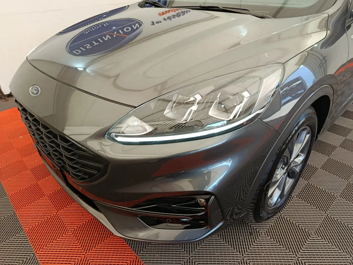 Vue 3/4 avant droit d'un Ford Kuga gris clair mettant en valeur ses phares LED et sa calandre noire.