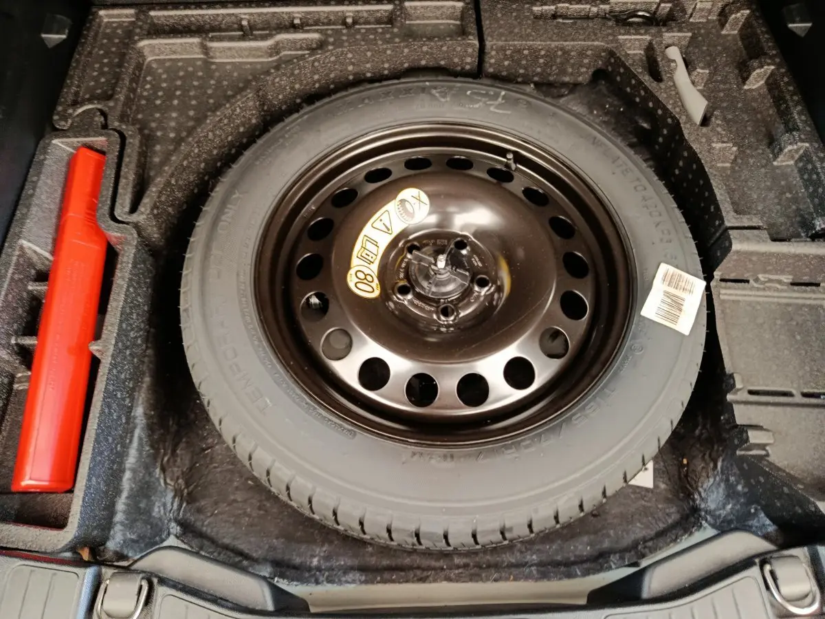 Vue plongeante sur la roue de secours noire et le rangement gris foncé du coffre du Ford Kuga gris clair 2024.