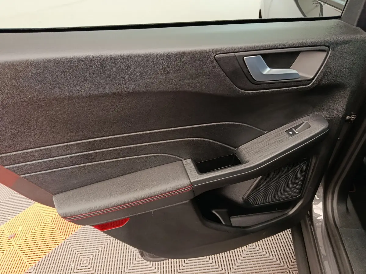 Vue côté gauche de la porte intérieure noire du Ford Kuga 2024 avec surpiqûres rouges et poignée argentée.