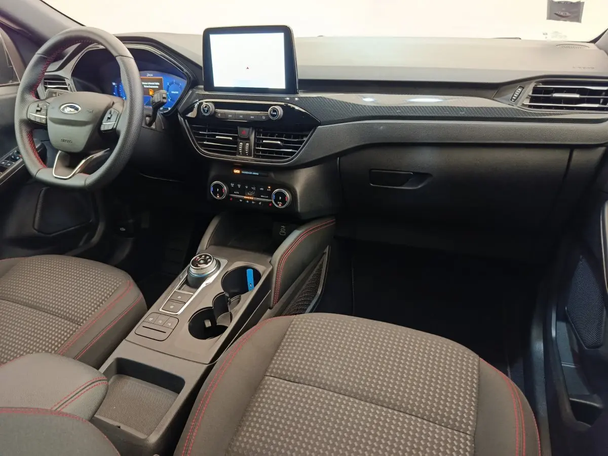 Intérieur avant du Ford Kuga 2024 gris clair, tableau de bord moderne avec écran tactile central et volant cuir noir.