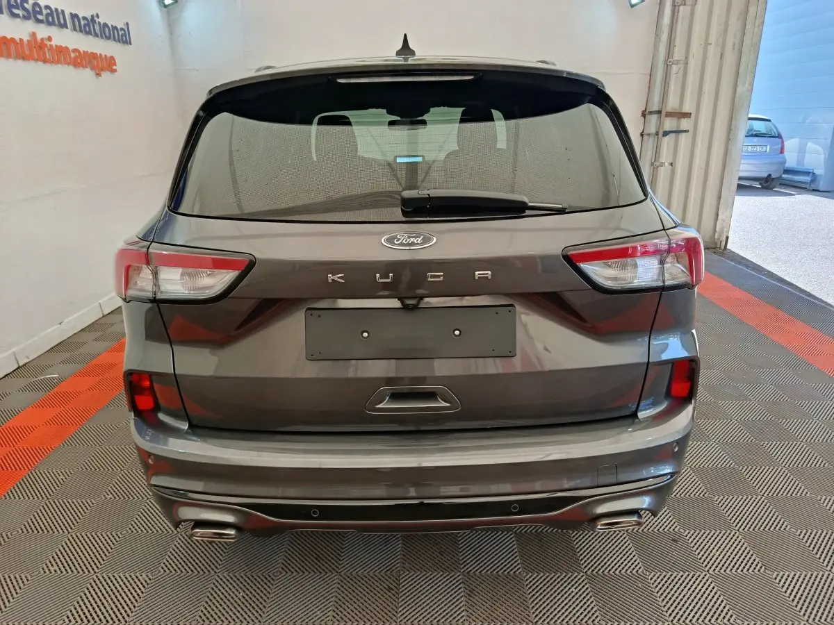 Vue arrière d'un Ford Kuga gris clair 2024 avec feux LED et double sortie d'échappement chromée dans un garage.