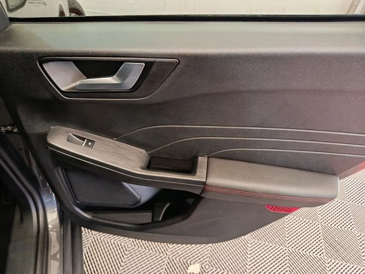 Gros plan sur la porte côté gauche du Ford Kuga gris clair, avec accoudoir noir et surpiqûres rouges visibles.