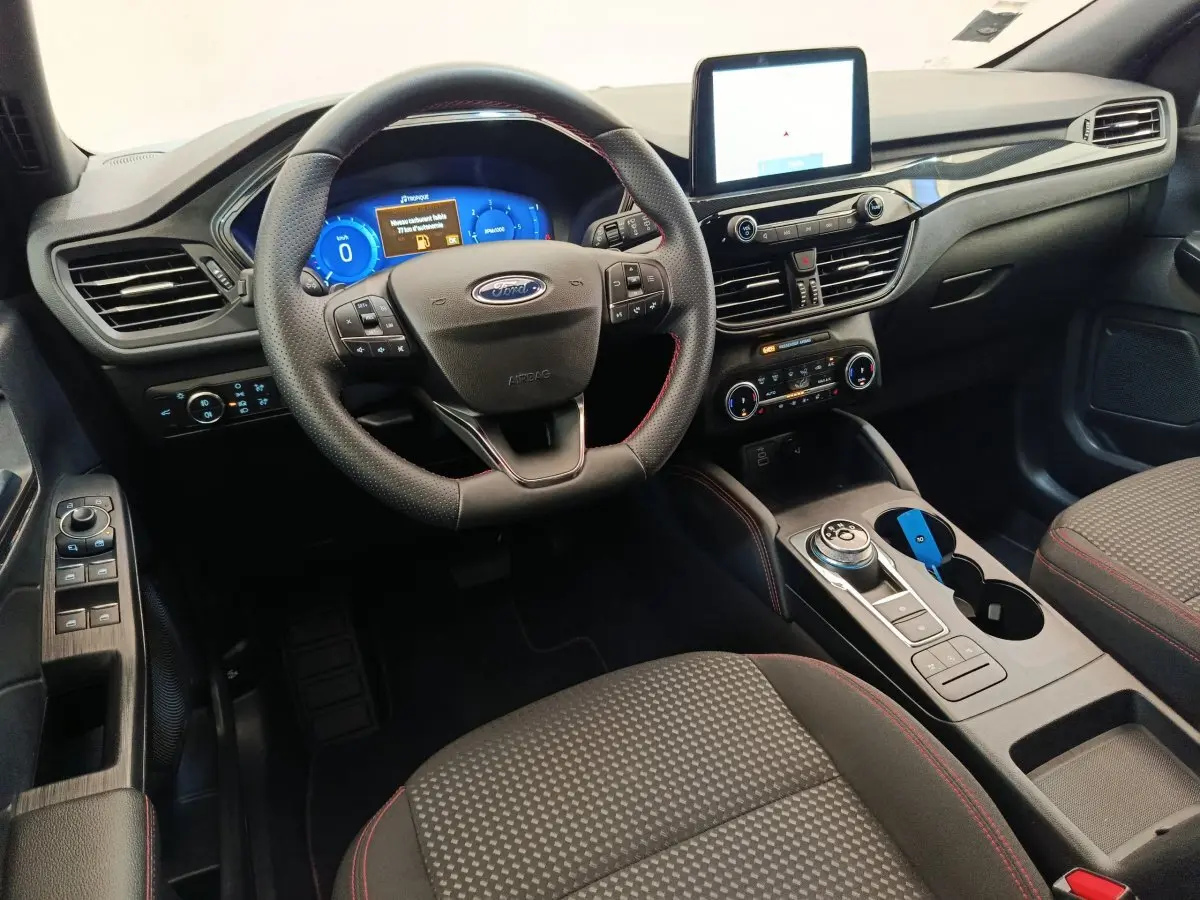 Vue intérieure avant du Ford Kuga 2024, tableau de bord noir avec écran tactile et volant cuir multifonctions.