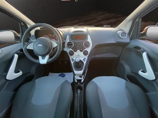 Vue intérieure avant de la Ford KA blanche 2015, tableau de bord avec console centrale et volant multifonction.