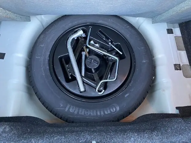 Vue plongeante sur la roue de secours noire et ses outils dans le coffre d'une Ford KA blanche de 2015.