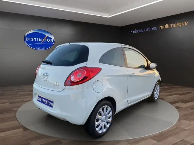 Vue 3/4 arrière droite d'une Ford KA blanche de 2015, compacte avec feux arrière ronds et jantes argentées.