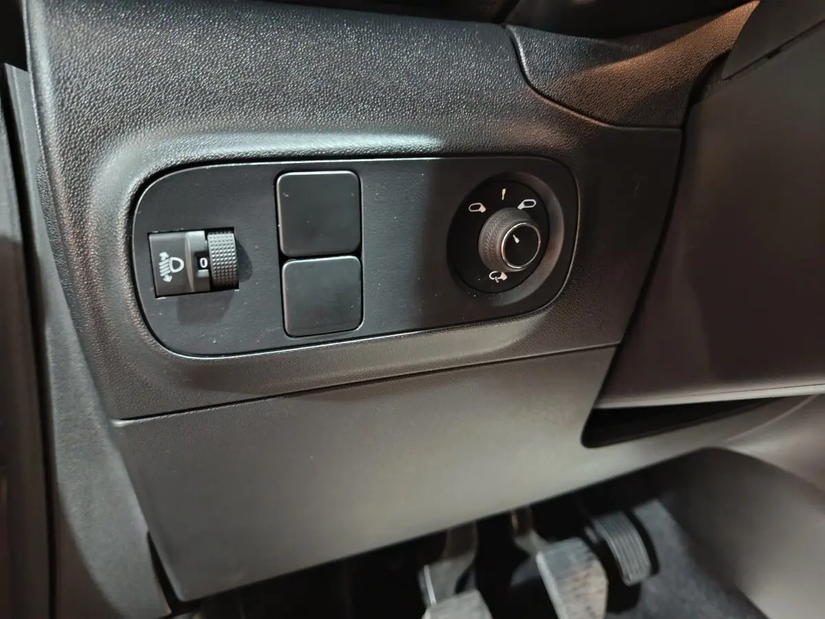 Gros plan sur les commandes de réglage des phares et des rétroviseurs côté conducteur d'une Citroën C3 gris foncé 2024.