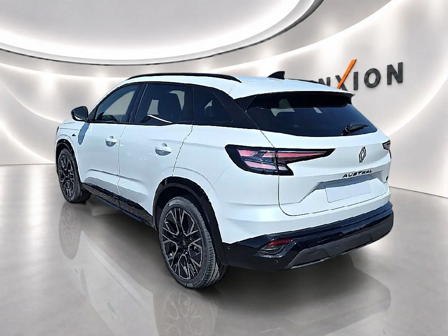Vue 3/4 arrière droite du Renault Austral blanc nacré avec jantes noires et toit noir contrasté dans un showroom.