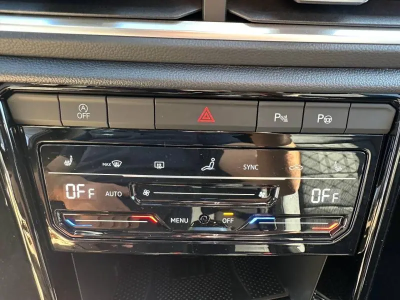 Gros plan sur la console centrale noire brillante du Volkswagen T-Roc 2025, affichant les commandes de climatisation et d'assistance.