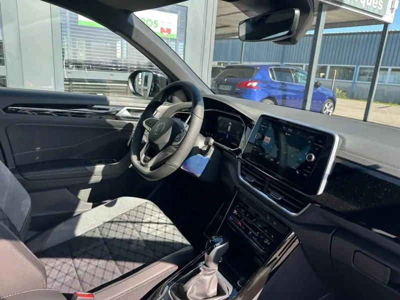 Vue intérieure côté conducteur du Volkswagen T-Roc 2025 noir nacré, avec volant cuir multifonction et écran tactile central.