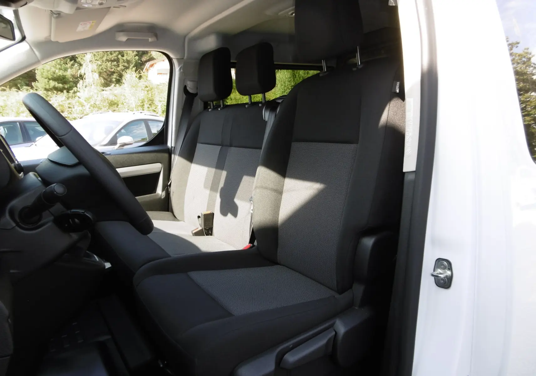 Intérieur du Peugeot Expert Long 2023, vue côté conducteur sur les sièges noirs en tissu et la portière blanche ouverte.