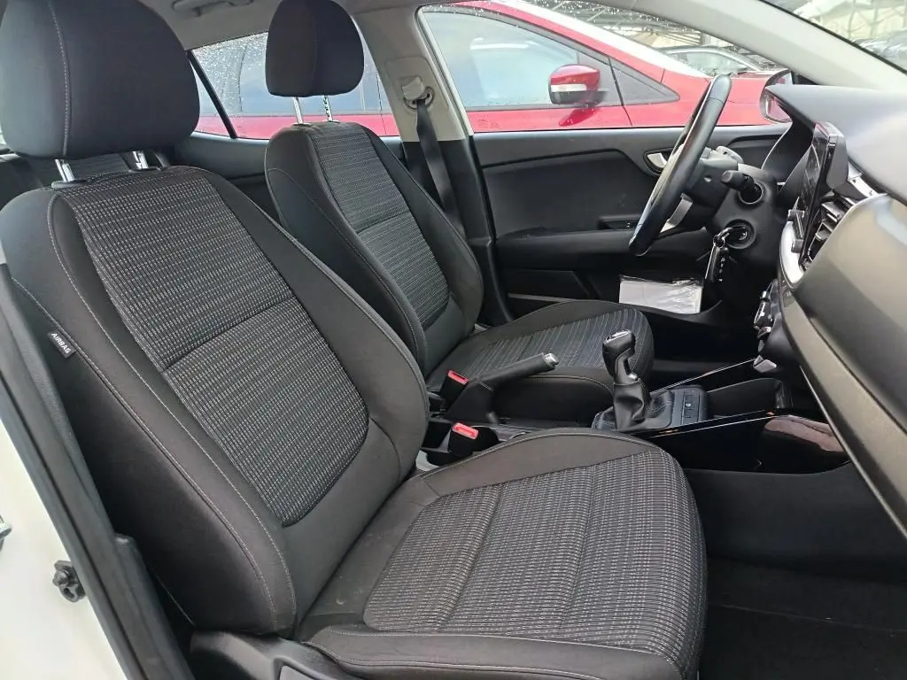 Vue intérieure côté conducteur du Kia Stonic blanc 2022, montrant les sièges tissu noirs et la boîte manuelle.