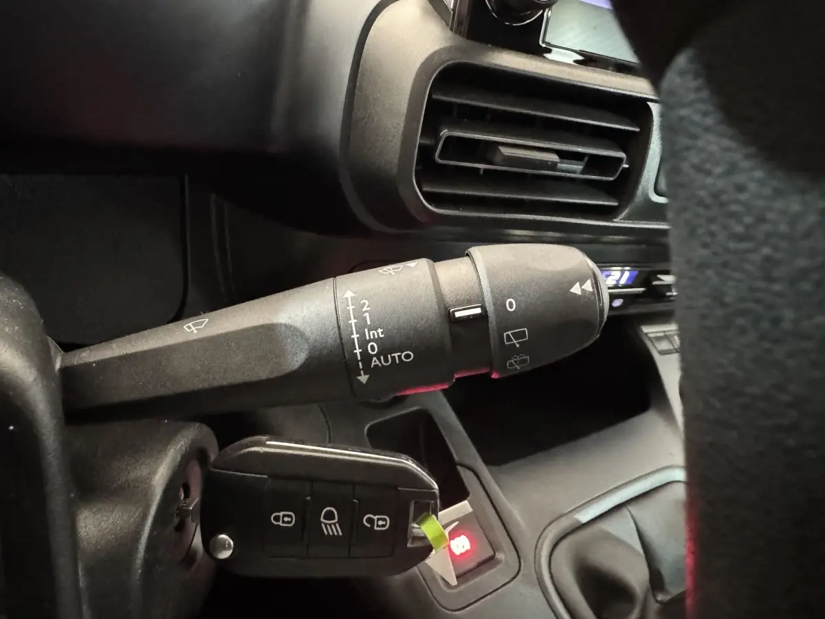 Gros plan sur la commande d’essuie-glace et la clé insérée du Peugeot Rifter blanc, tableau de bord partiellement visible.