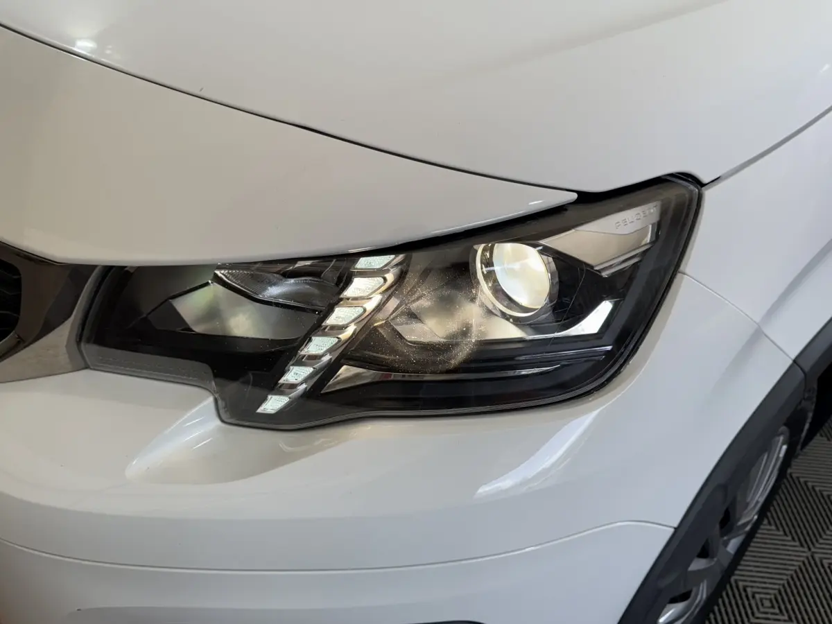 Gros plan sur le phare avant droit du Peugeot Rifter blanc, mettant en valeur les LED diurnes et la carrosserie lisse.