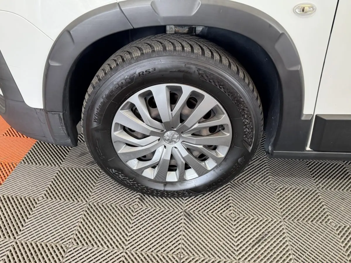 Gros plan sur la roue avant droite d’un Peugeot Rifter blanc, avec jante argentée et pneu hiver Hankook.