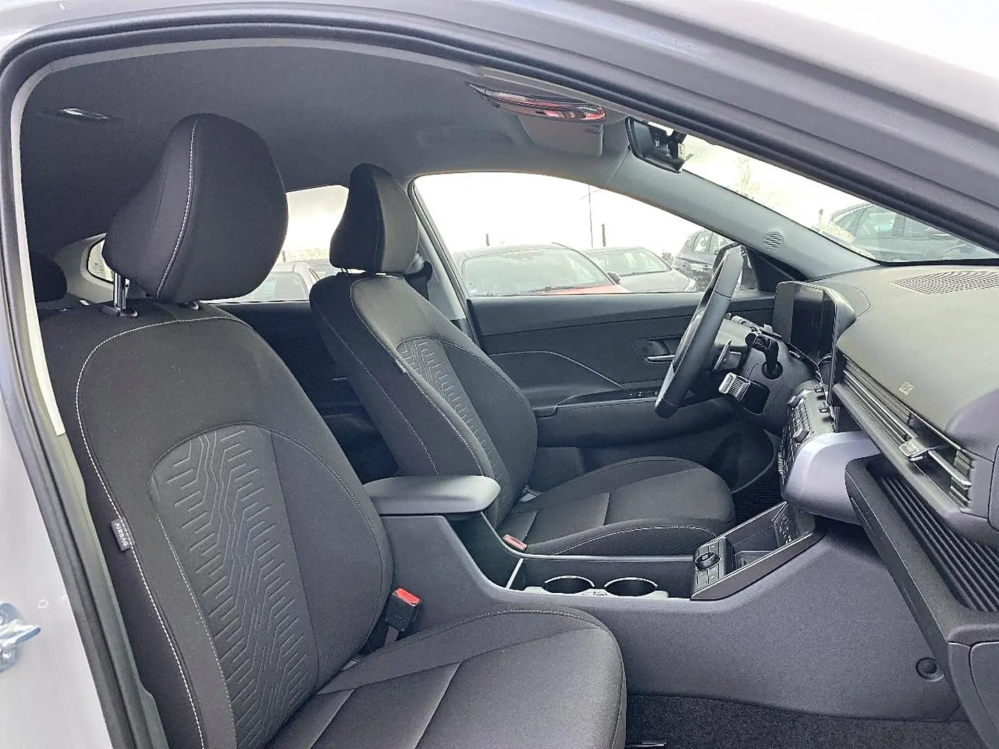 Intérieur de la Hyundai Kona 2025 vue côté conducteur, sièges tissu noirs avec accoudoir central et tableau de bord moderne.