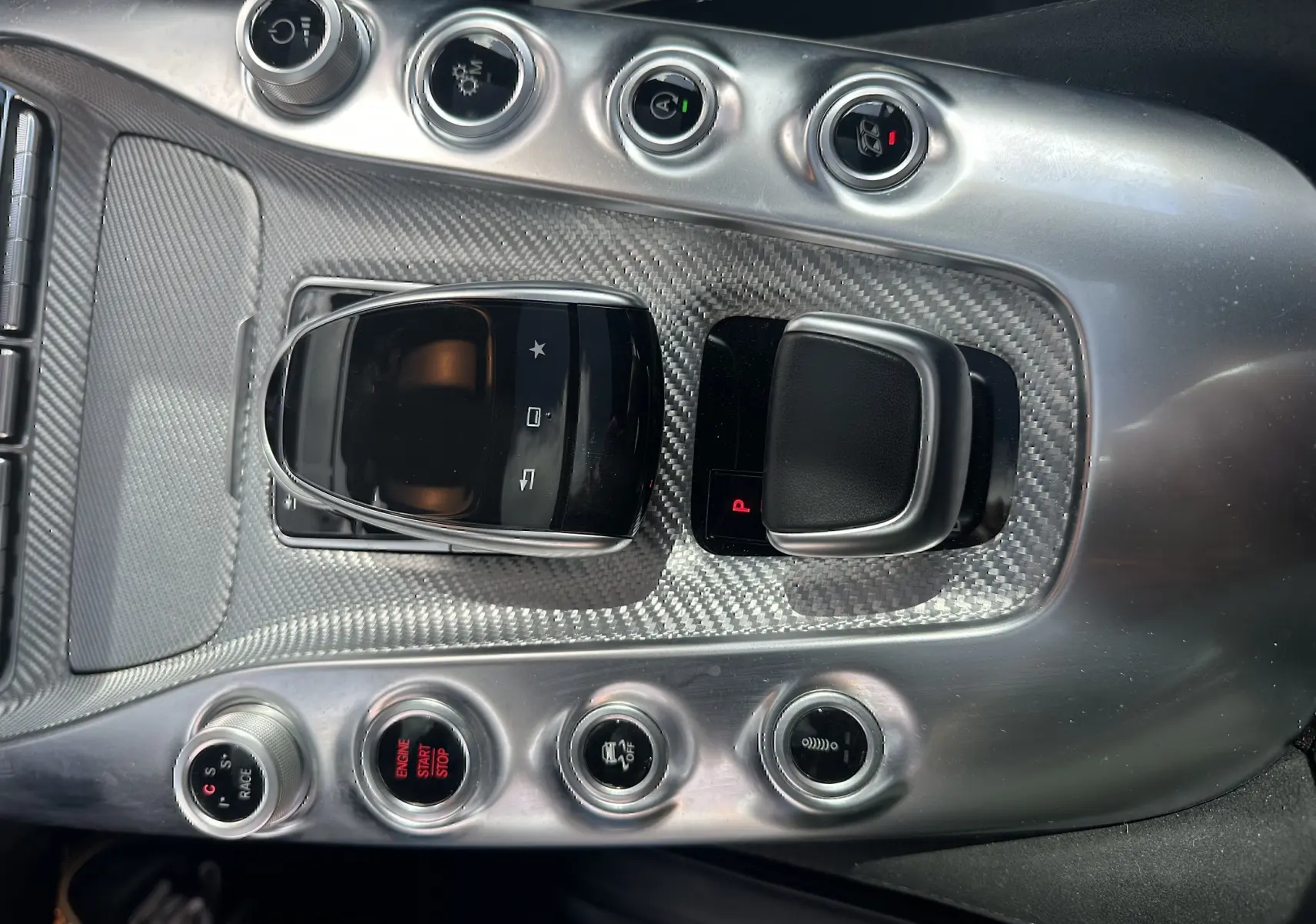 Gros plan sur la console centrale en fibre de carbone du Mercedes AMG GT gris foncé, avec commandes de boîte auto et boutons de fonction.