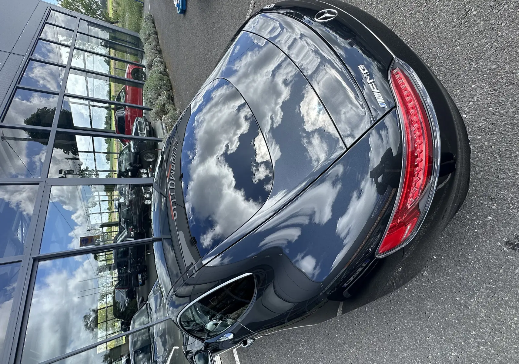 Vue 3/4 arrière d'une Mercedes AMG GT gris foncé brillant, avec feux arrière LED et logo AMG visible.