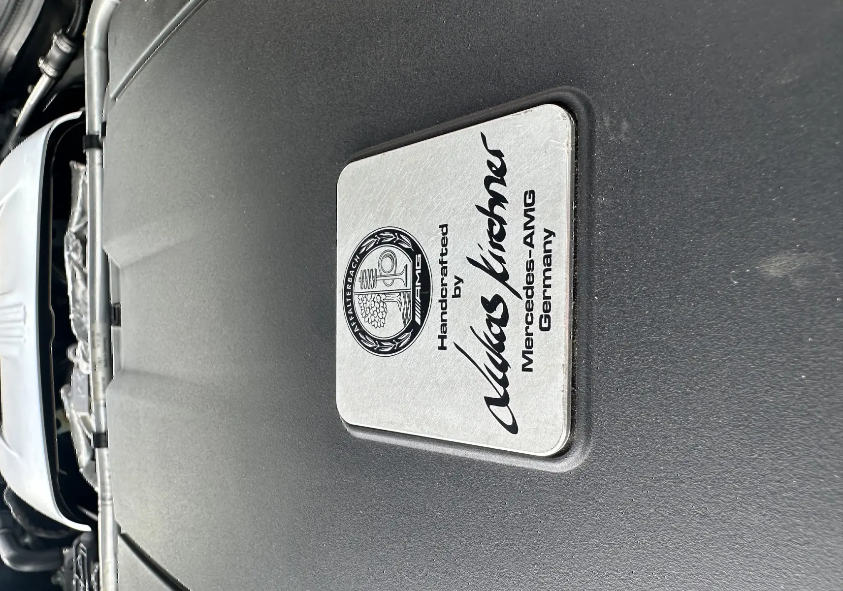 Gros plan sur la plaque du moteur gris foncé d'une Mercedes AMG GT 4.0 V8 510 S, soulignant l'artisanat allemand.