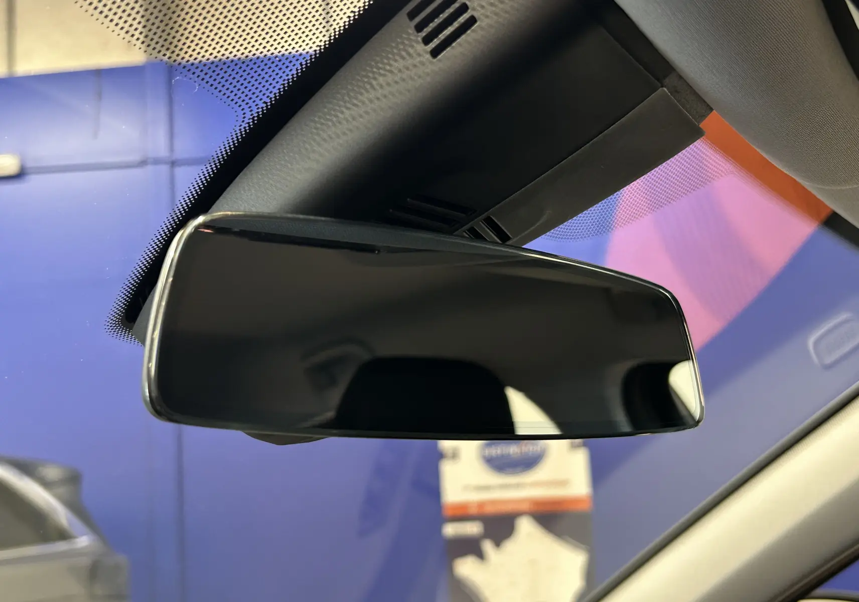 Rétroviseur intérieur noir de la BMW Série 1 16d 2023, vue rapprochée avec pare-brise et ciel bleu en arrière-plan.