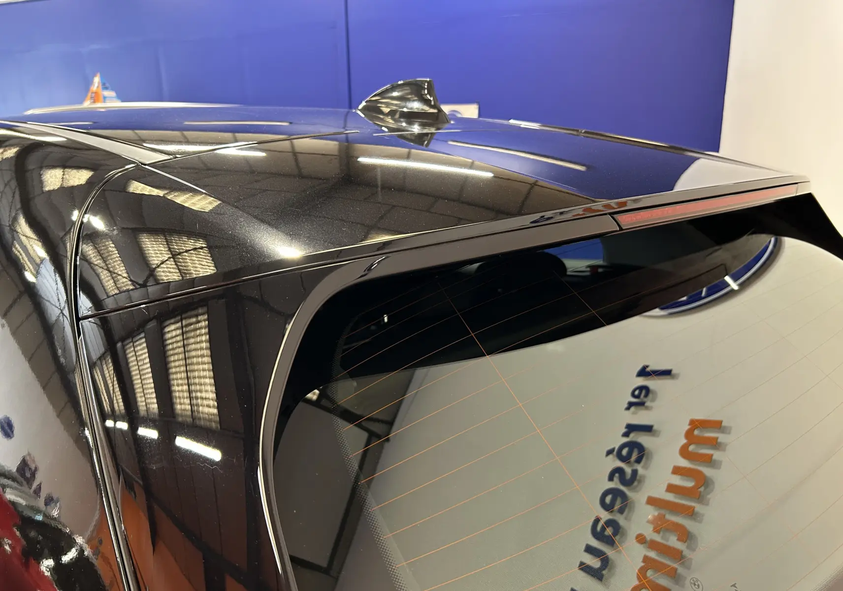 Gros plan sur l'angle arrière droit d'une BMW Série 1 noire 2023, mettant en valeur l'antenne requin et la lunette arrière teintée.