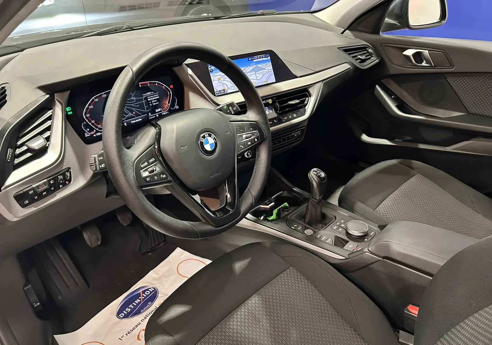 Intérieur côté conducteur de la BMW Série 1 16d noire 2023, tableau de bord numérique et écran GPS visible.