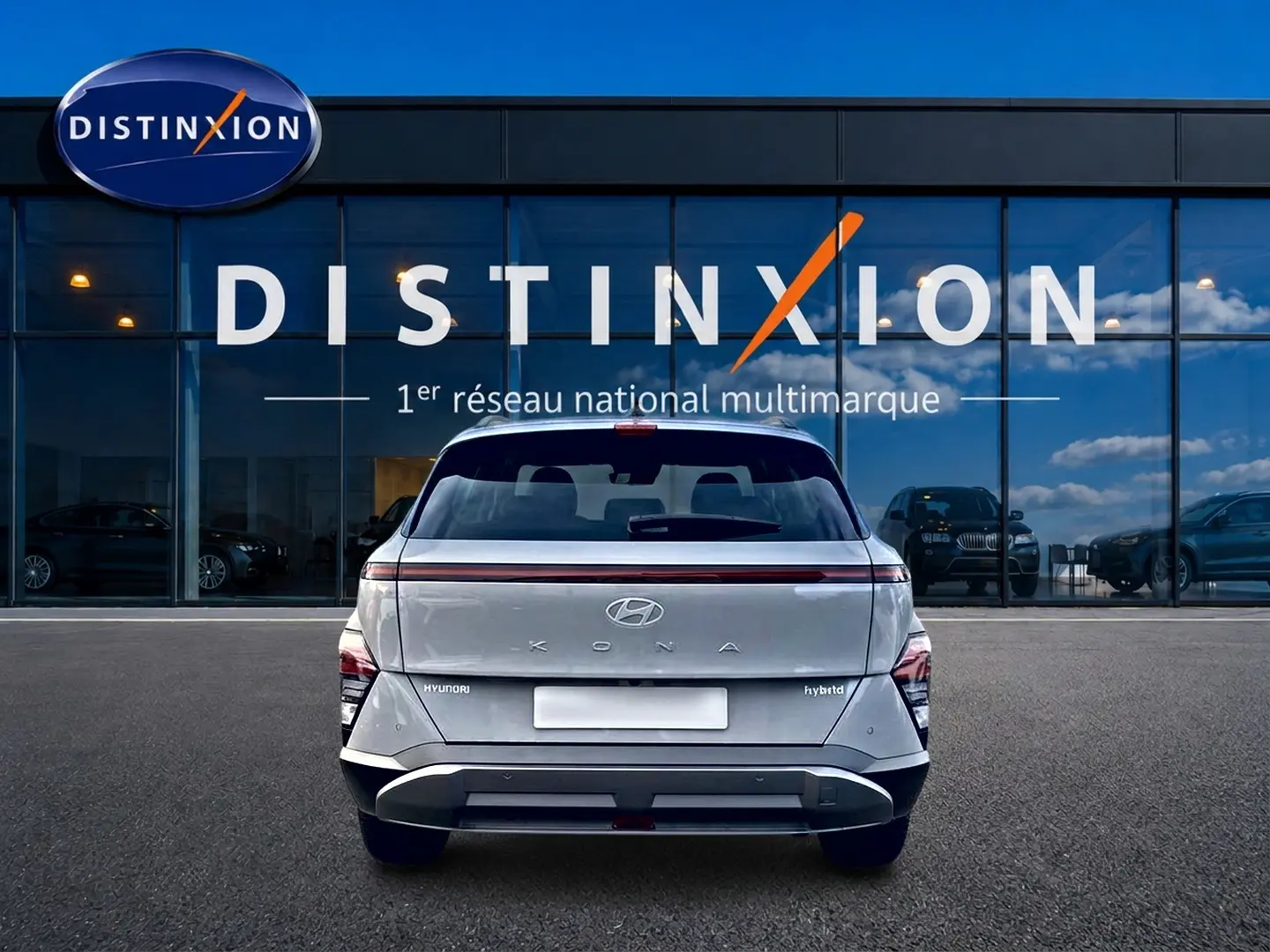 Vue arrière d'un Hyundai Kona gris 2025 avec feux arrière LED et bande lumineuse rouge, devant une vitrine Distinxion.