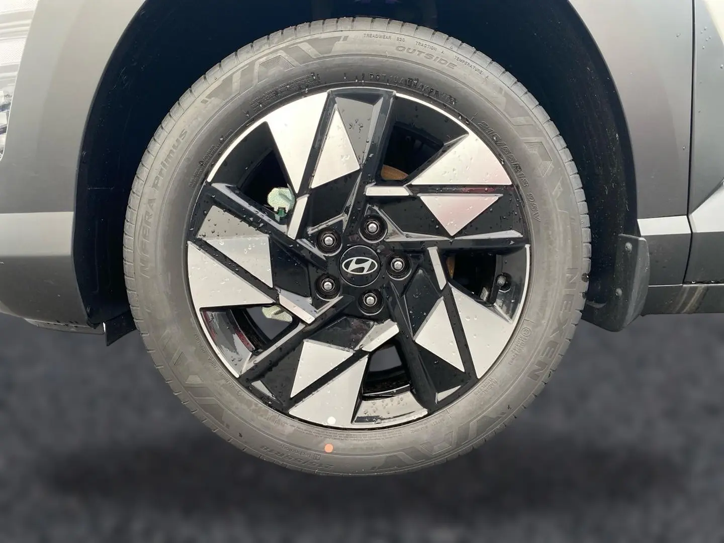 Gros plan sur la roue avant gauche du Hyundai Kona gris 2025 avec jante alliage noire et argentée au design géométrique.