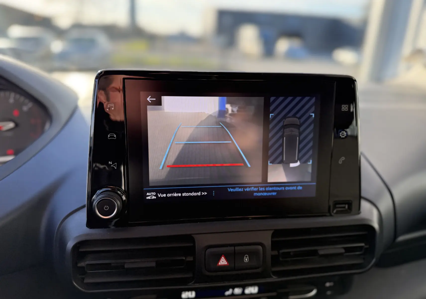 Écran central du Peugeot Rifter gris platinium montrant la caméra de recul avec guidage et vue aérienne du véhicule.