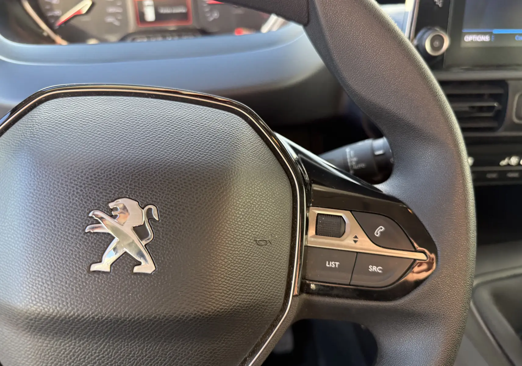 Gros plan sur le volant noir du Peugeot Rifter 2020 avec commandes intégrées côté droit et logo lion argenté.