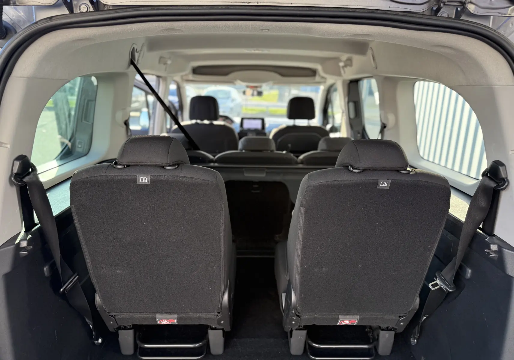 Vue intérieure arrière du Peugeot Rifter gris, montrant les sièges arrière en tissu et l'espace passagers sur 7 places.
