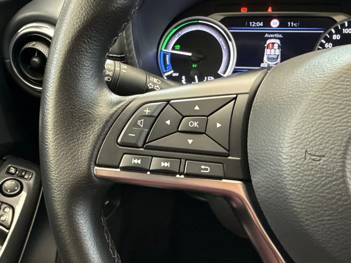 Gros plan sur le volant noir du Nissan Juke 2023 avec commandes multifonctions et tableau de bord numérique en arrière-plan.