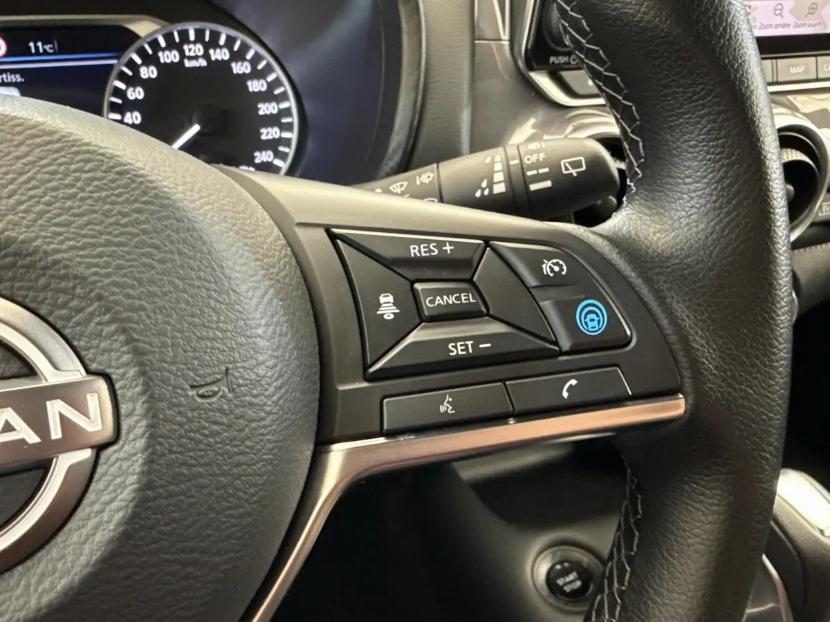 Gros plan sur le volant noir du Nissan Juke 2023, montrant les commandes du régulateur de vitesse et assistance au freinage.