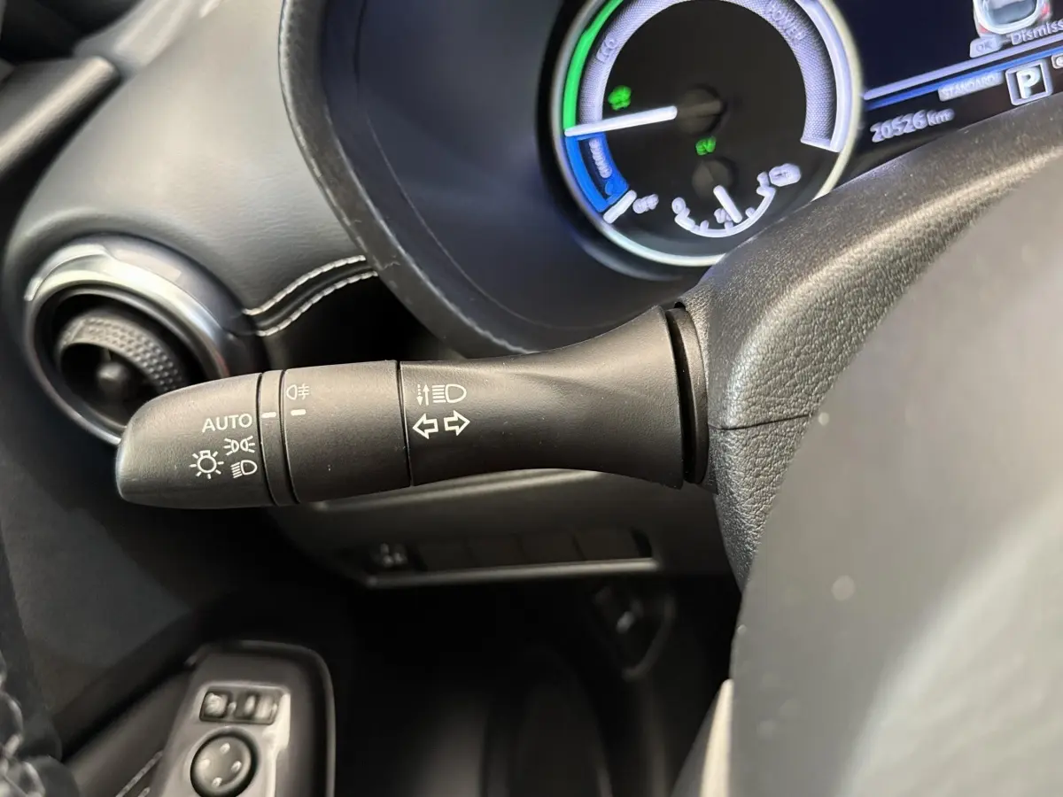 Gros plan sur la manette de clignotants et phares du tableau de bord d’un Nissan Juke gris foncé 2023.