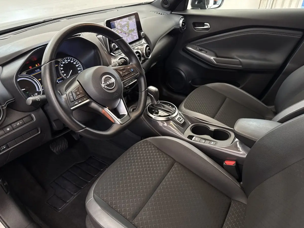 Intérieur du Nissan Juke 2023 vu côté conducteur, montrant volant multifonctions, écran tactile et sièges tissu gris foncé.